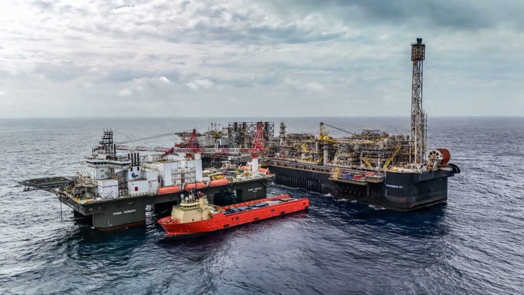Plataforma de petróleo "PETROBRAS 67" e navios de apoio "POSH XANADU" e um navio vermelho em alto mar sob céu nublado.