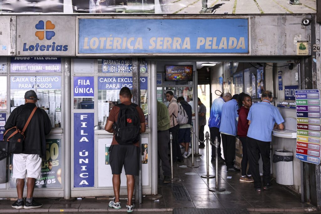 Pessoas aguardam em fila na entrada de uma casa lotérica com a placa "Lotérica Serra Pelada".