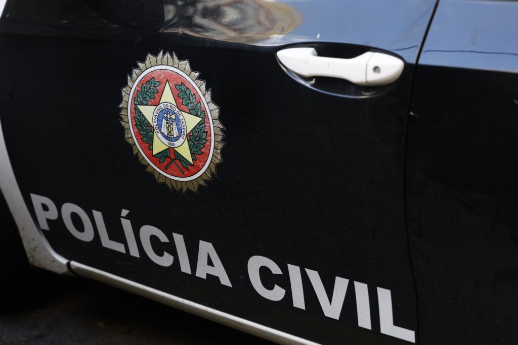 Detalhe de viatura preta com a inscrição "POLÍCIA CIVIL" e o brasão da Polícia Civil do Rio de Janeiro.