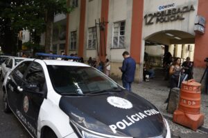 Viatura da Polícia Civil estacionada em frente à "12ª Delegacia Policial", com pessoas reunidas na calçada.