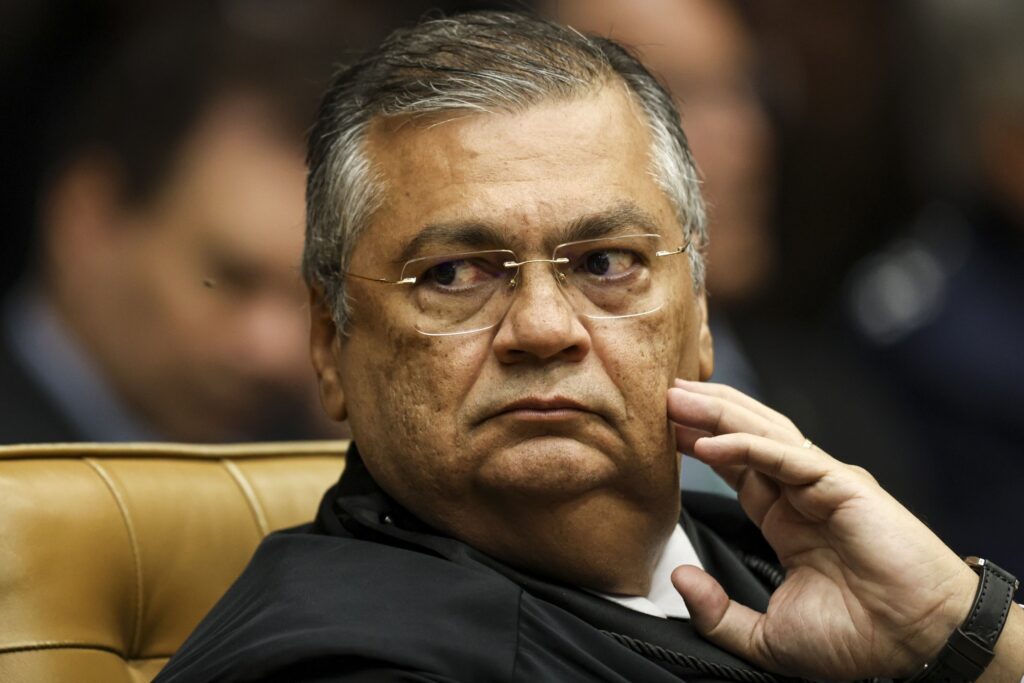 Plano fechado do ministro do STF, Flávio Dino, vestindo toga e com expressão séria.