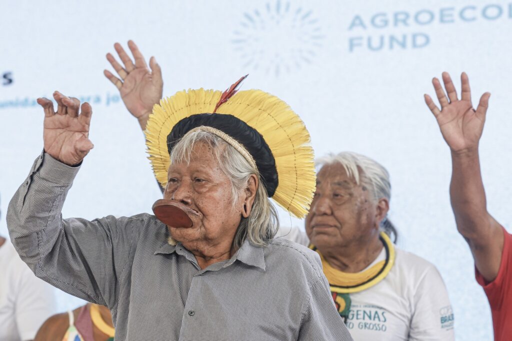 Cacique Raoni Metuktire, com adorno labial e cocar amarelo, levanta as mãos durante a cúpula dos povos.