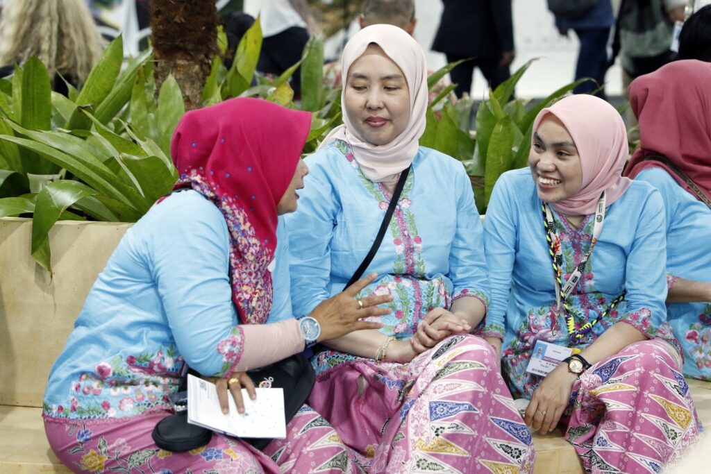 Três mulheres com hijabs e vestimentas tradicionais azuis e rosas conversam sentadas em um banco na COP30.