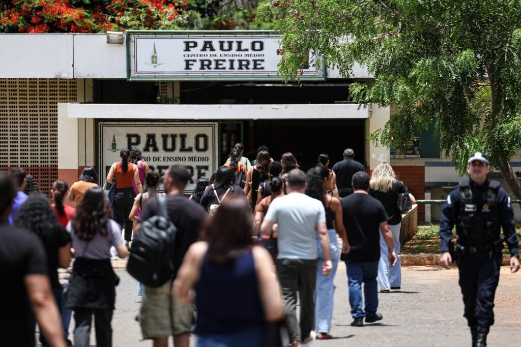 Pessoas caminham em direção à entrada do Centro de Ensino Médio "Paulo Freire" para a realização de provas.