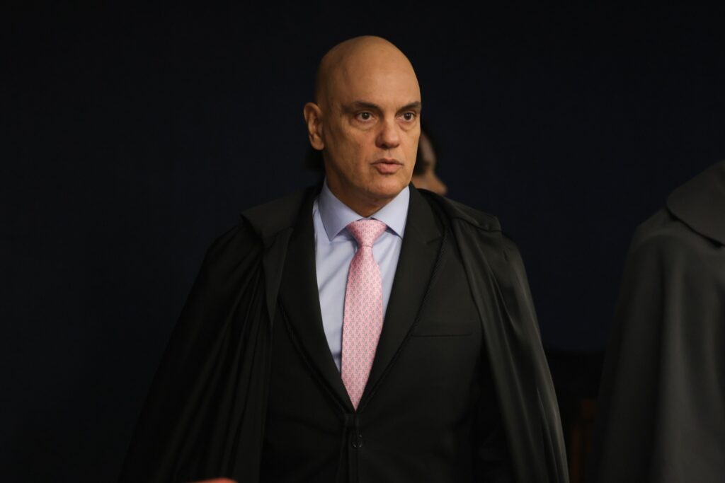O ministro Alexandre de Moraes veste toga preta, camisa azul e gravata rosa.