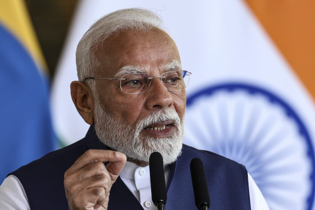 Narendra Modi, primeiro-ministro da Índia, fala ao microfone com a bandeira da Índia ao fundo.