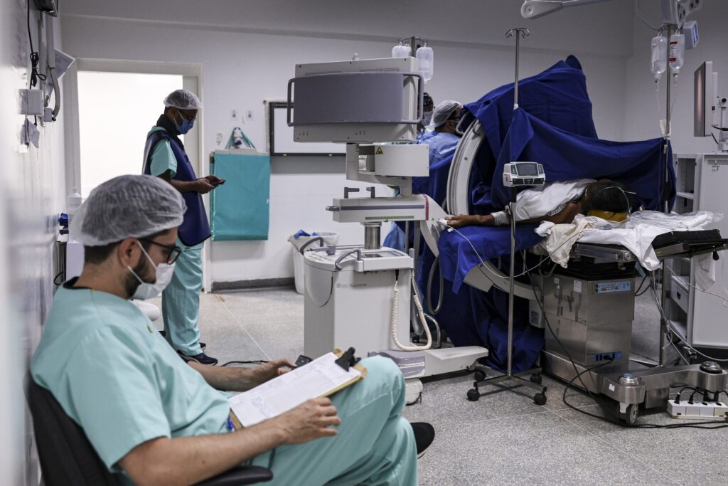 Profissionais de saúde em sala de cirurgia ao lado de um paciente e de um aparelho de imagem médica "OEC Fluorostar".