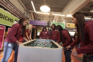 Cinco jovens atletas com uniformes do São Paulo FC jogam pebolim em uma exposição no Museu do Futebol.
