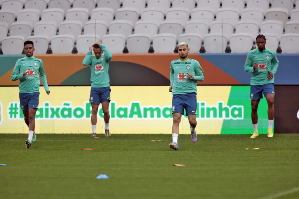 Quatro jogadores da Seleção Brasileira de Futebol correm durante treino em um campo de estádio.