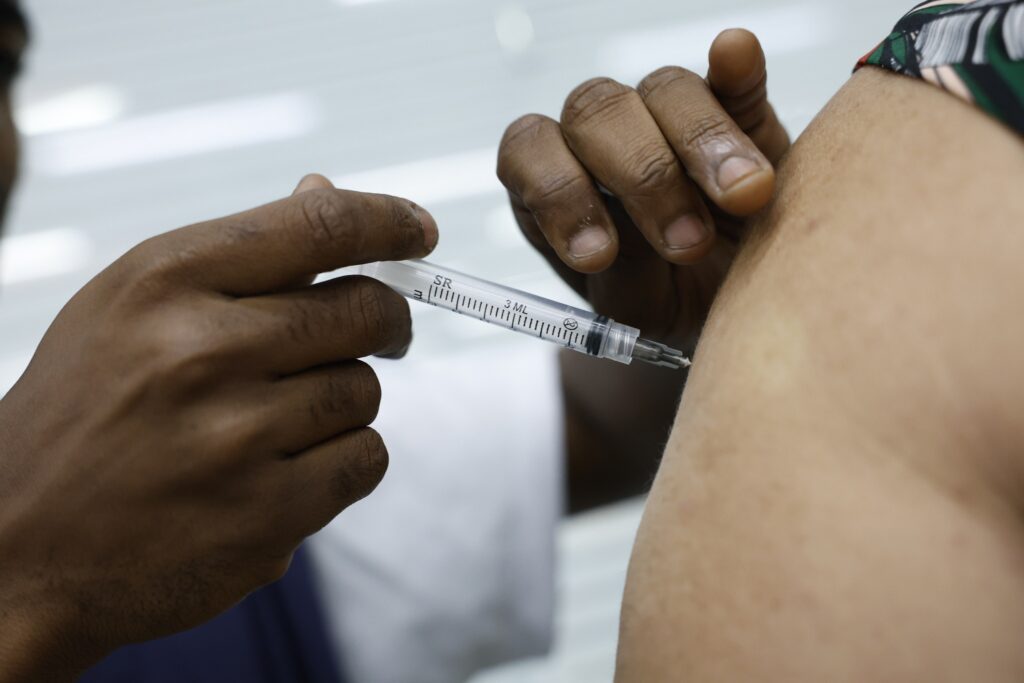 Profissional de saúde aplica vacina no braço de um paciente.