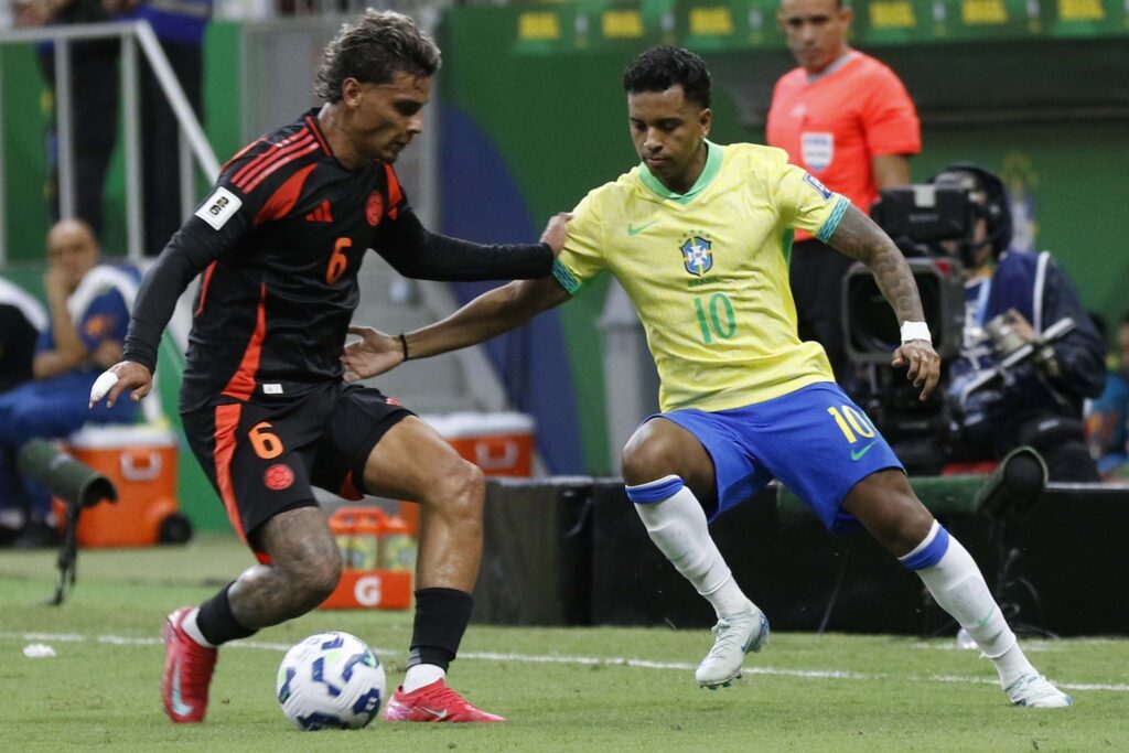 Jogador da seleção do Brasil com a camisa "10" disputa a bola com jogador da seleção da Colômbia com a camisa "6" durante partida de futebol.