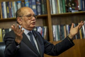 Gilmar Mendes (ministro do Supremo Tribunal Federal) gesticulando com as mãos durante entrevista em frente a uma estante de livros.