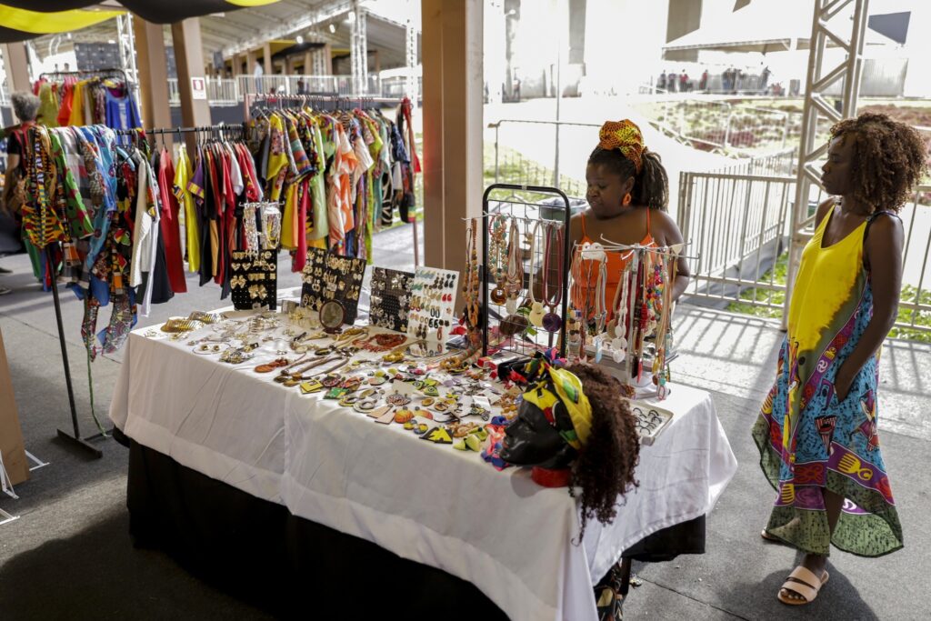 Duas mulheres negras em uma feira de artesanato e roupas coloridas em evento do Dia da Consciência Negra.