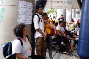 Jovens candidatos aguardam a primeira etapa do Enem 2024 ao lado de listas de salas do 'Cebraspe'.
