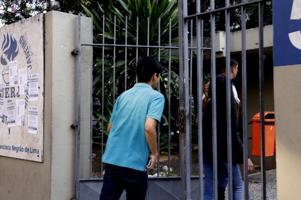 Pessoas entram por um portão metálico na UERJ para a realização de provas do Concurso Público Nacional Unificado.