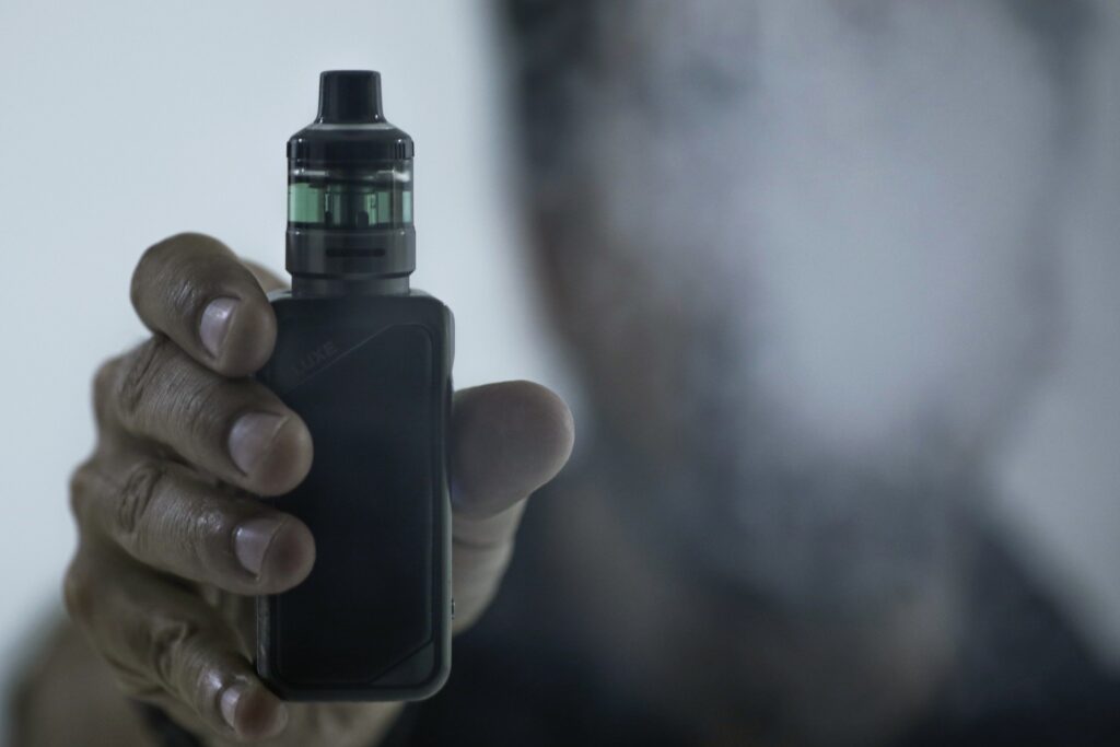 Uma mão segura um cigarro eletrônico preto com líquido verde no reservatório.