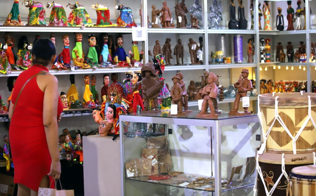 Uma mulher de vestido vermelho observa bonecos e figuras de artesanato em exposição.