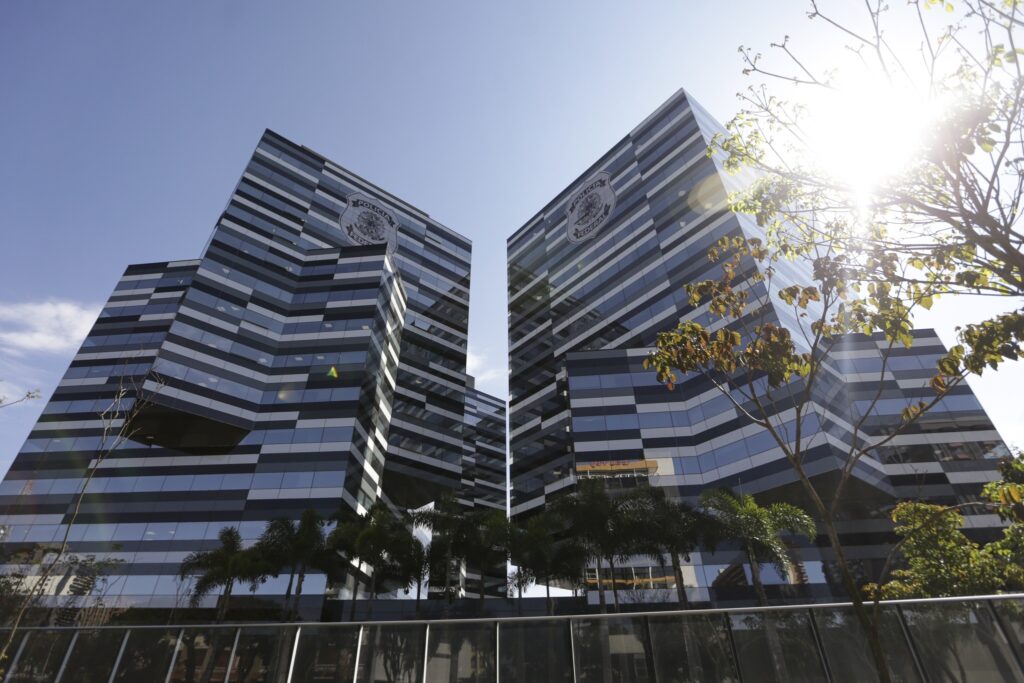 Fachada dos prédios da "Polícia Federal" em Brasília, com arquitetura moderna de vidros listrados e palmeiras ao redor.