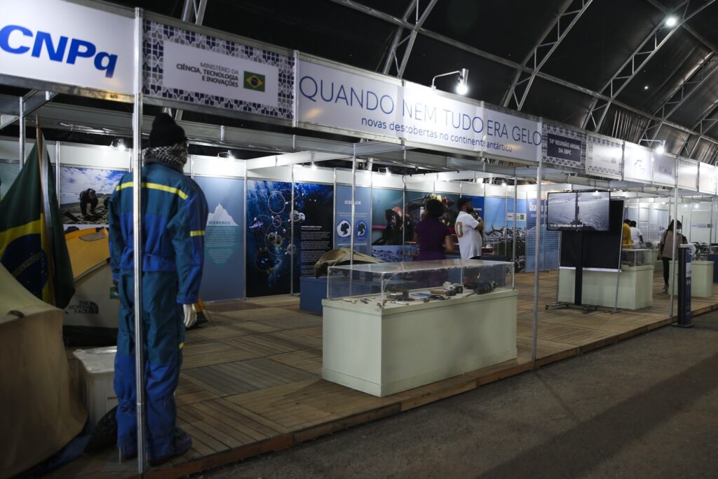 Estande da exposição "Quando nem tudo era gelo - novas descobertas no continente antártico", com manequim em traje térmico, painéis informativos e visitantes.