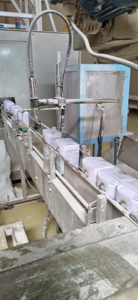 Pacotes brancos em uma esteira de produção industrial coberta por pó branco, com a inscrição "INFORMAÇÃO NUTRICIONAL".