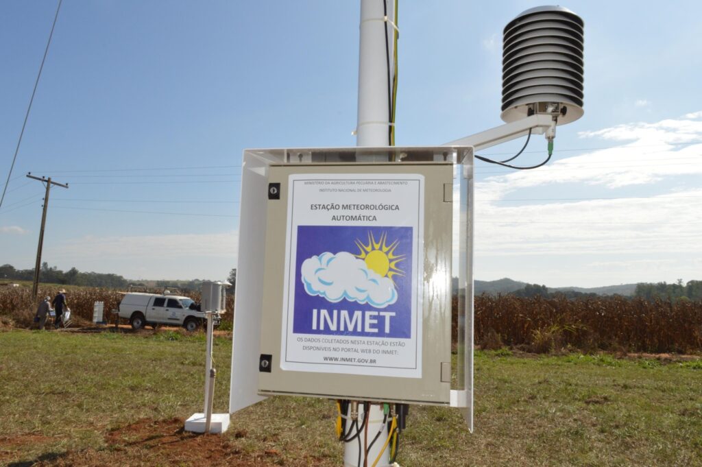 Estação Meteorológica Automática do INMET instalada em campo, com placa informativa e sensores.