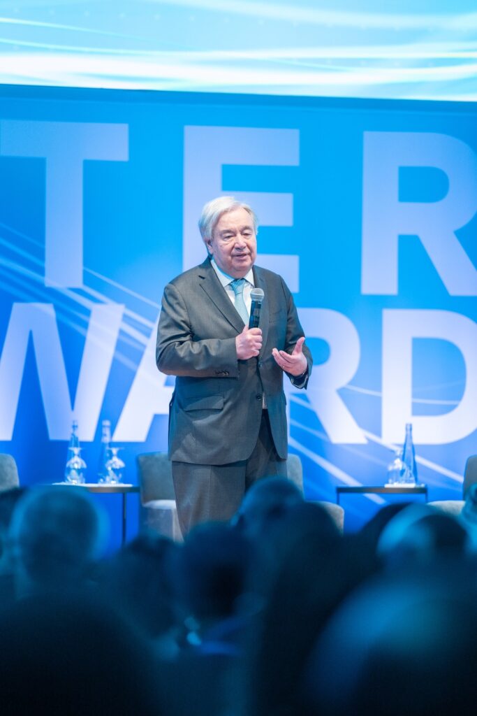 António Guterres discursa em evento com painel azul ao fundo com a inscrição "WATER FORWARD".