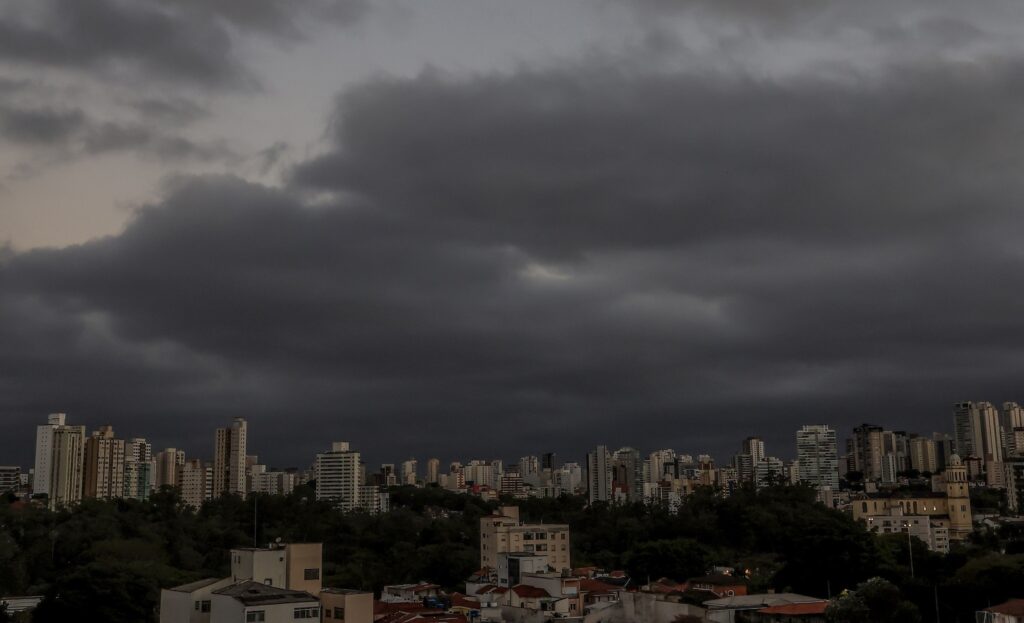 Vista panorâmica de edifícios urbanos sob céu coberto por nuvens escuras de temporal.