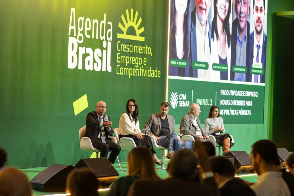 Participantes sentados em painel de debate do evento Agenda Brasil com projeção ao fundo.