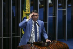 Senador Flávio Bolsonaro discursa na tribuna do Senado Federal, com a mão direita na testa.