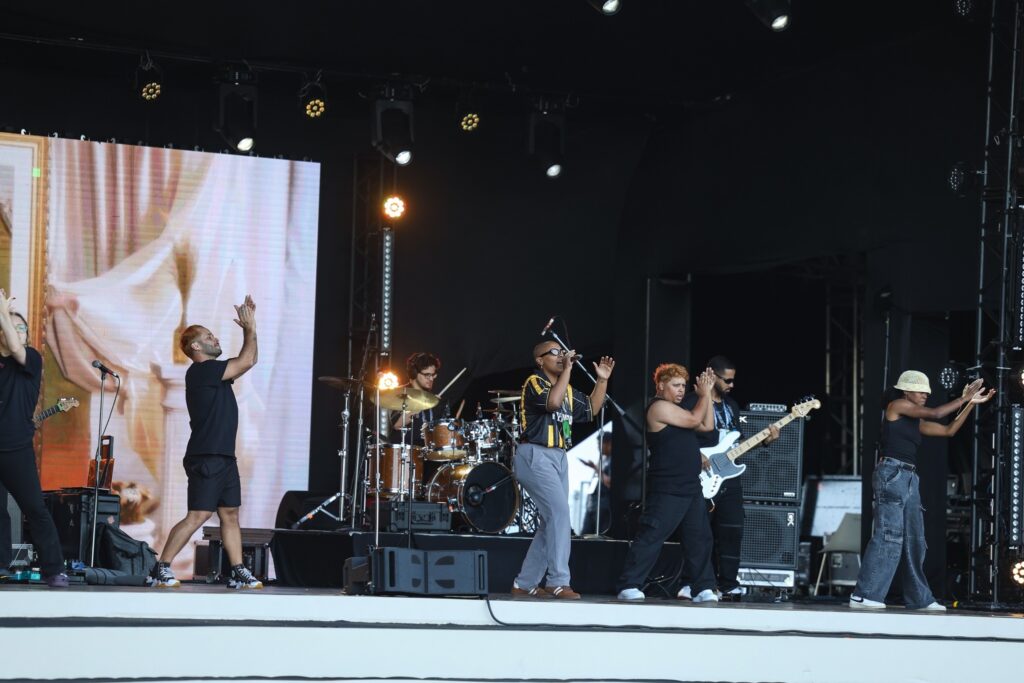 Banda musical se apresenta em palco com grande telão ao fundo.