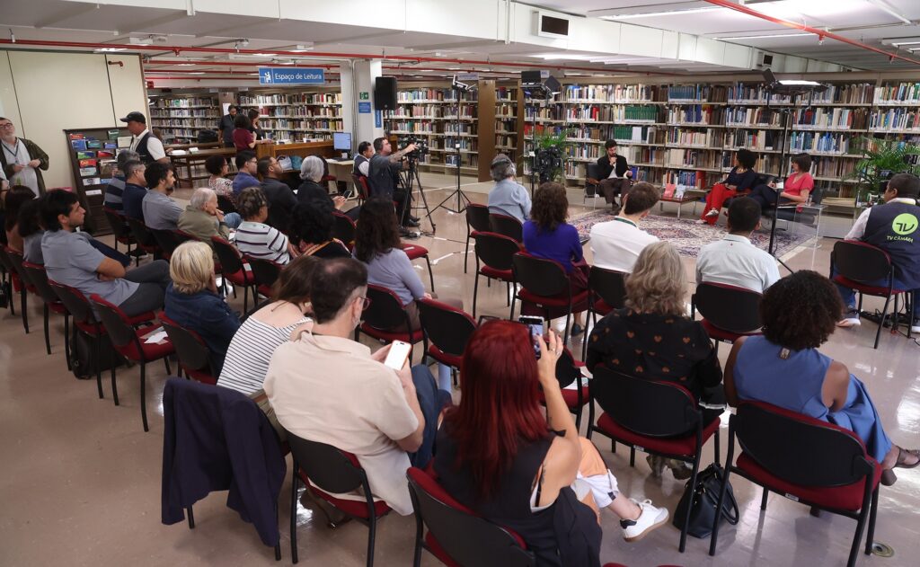 Público assiste a bate-papo com autor em evento literário dentro de biblioteca.