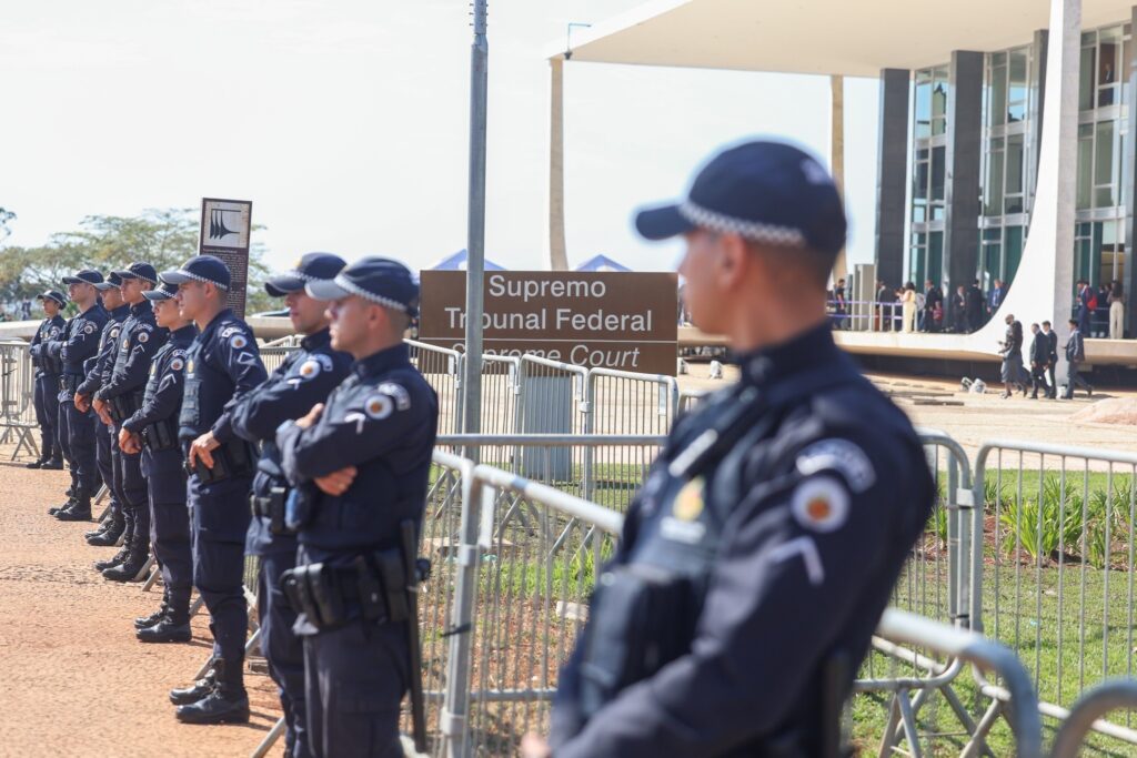 Agentes de segurança em uniformes azul-marinho posicionados atrás de grades metálicas em frente ao edifício do Supremo Tribunal Federal, com uma placa indicando "Supremo Tribunal Federal".