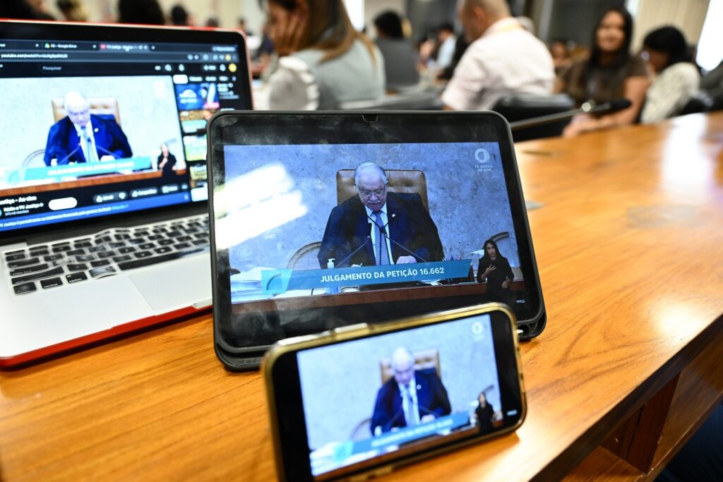 Telas de notebook, tablet e smartphone sobre uma mesa exibem transmissão ao vivo de sessão do Supremo Tribunal Federal com o texto "JULGAMENTO DA PETIÇÃO 16.662".