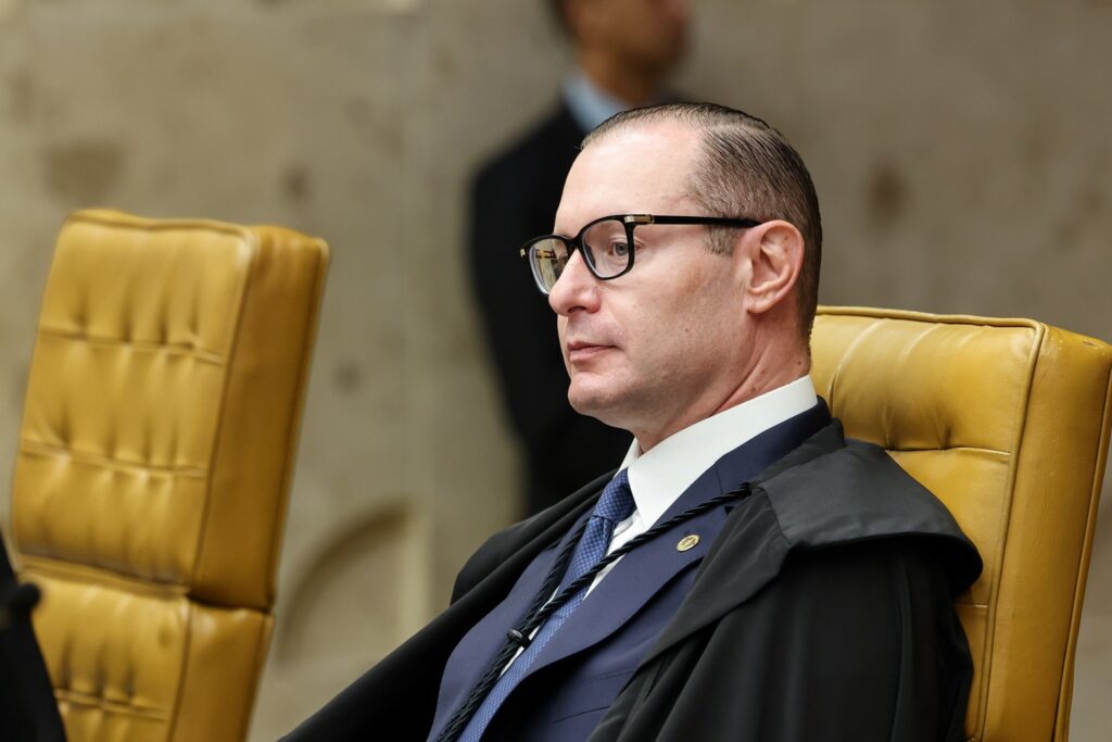 O ministro Cristiano Zanin (ministro do Supremo Tribunal Federal) está sentado em uma poltrona amarela, vestindo terno, toga preta e óculos.