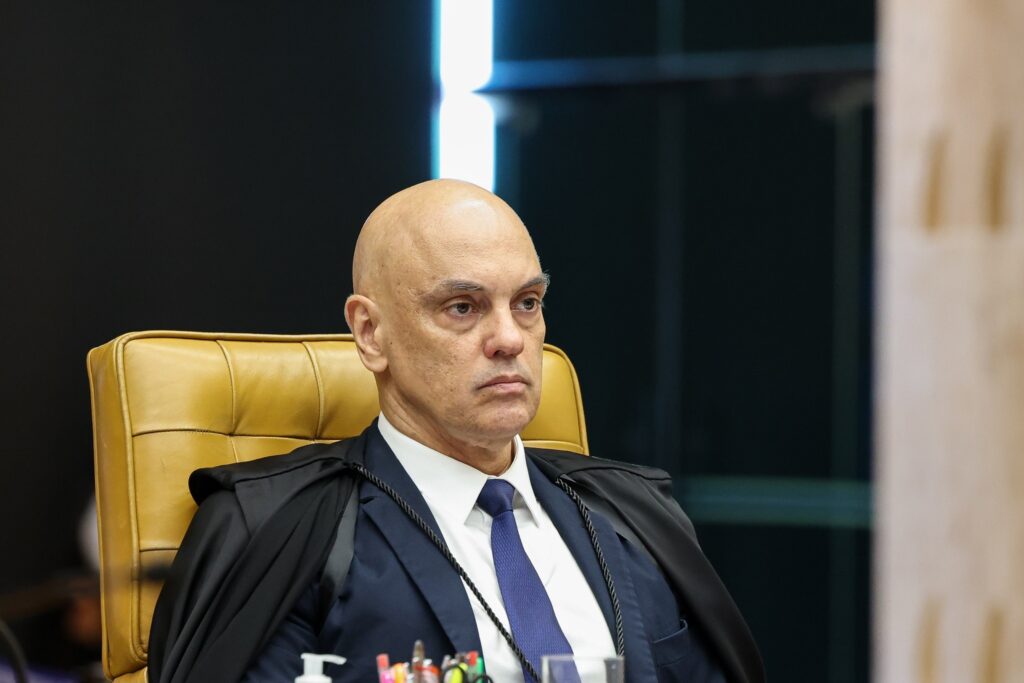 O ministro Alexandre de Moraes, com expressão séria, veste toga preta e gravata azul em sessão do STF.