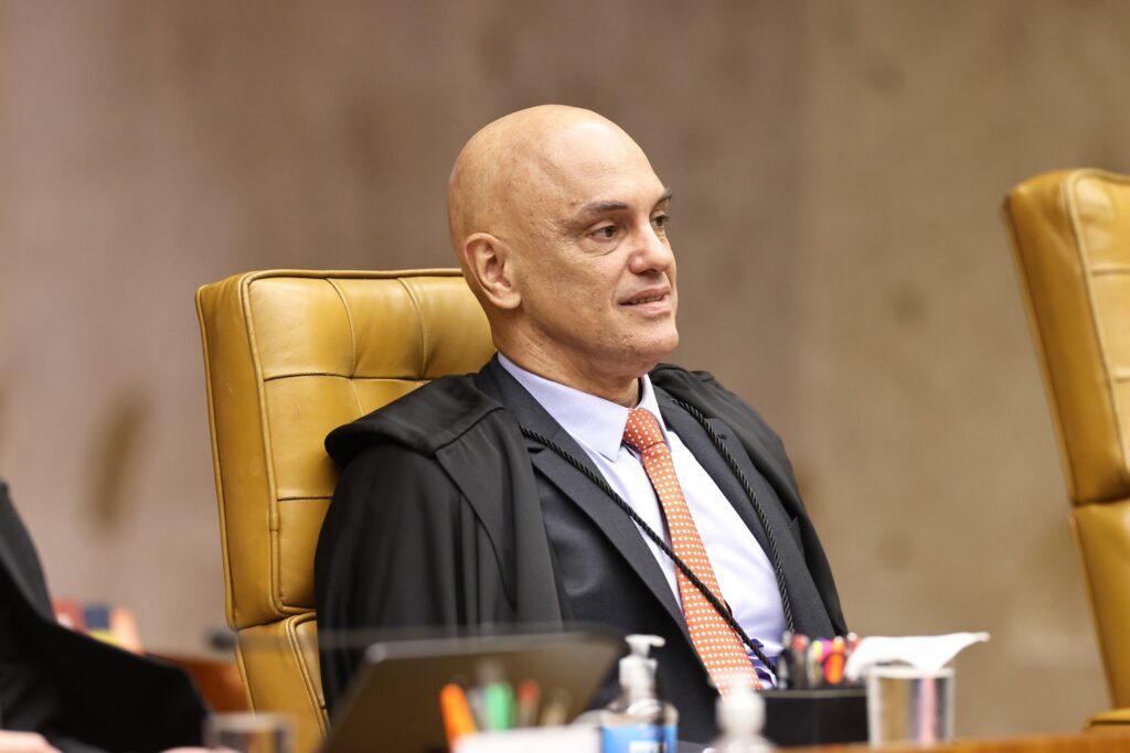 O ministro Alexandre de Moraes, de toga preta e gravata alaranjada, sentado em poltrona no plenário do STF.
