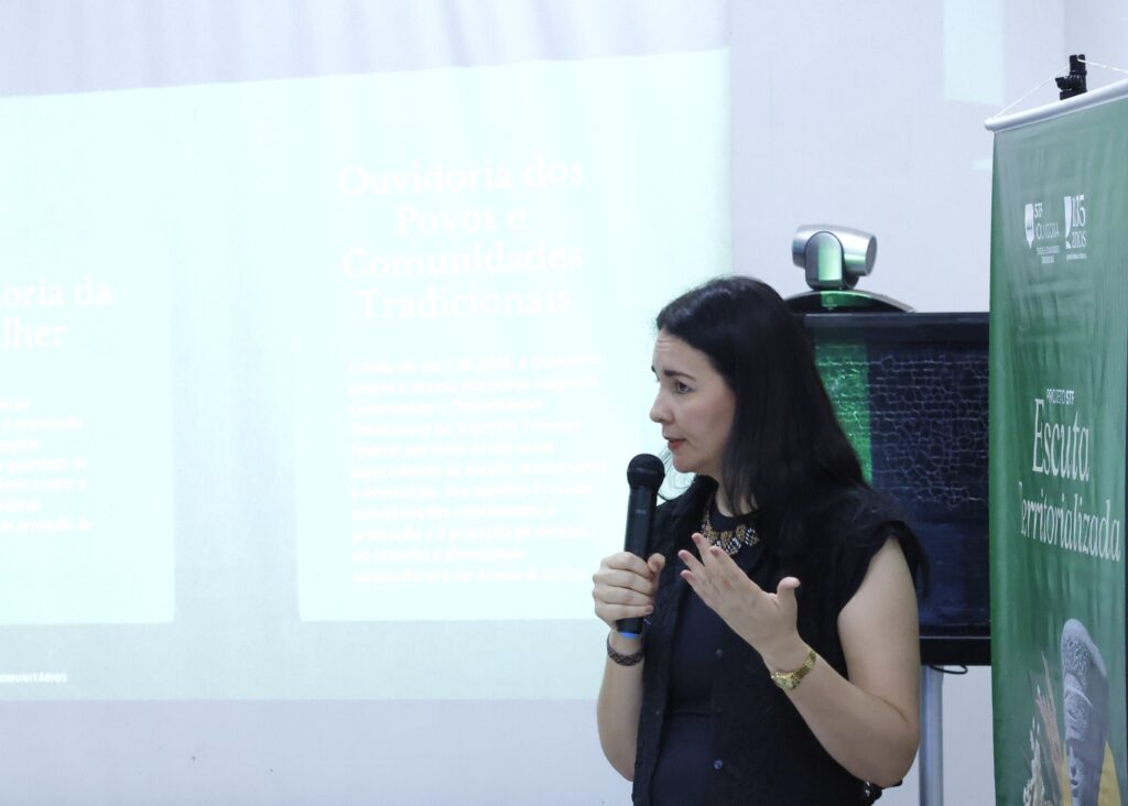 Mulher fala ao microfone durante o "Projeto STF Escuta Territorializada", com projeção ao fundo mencionando a "Ouvidoria dos Povos e Comunidades Tradicionais".
