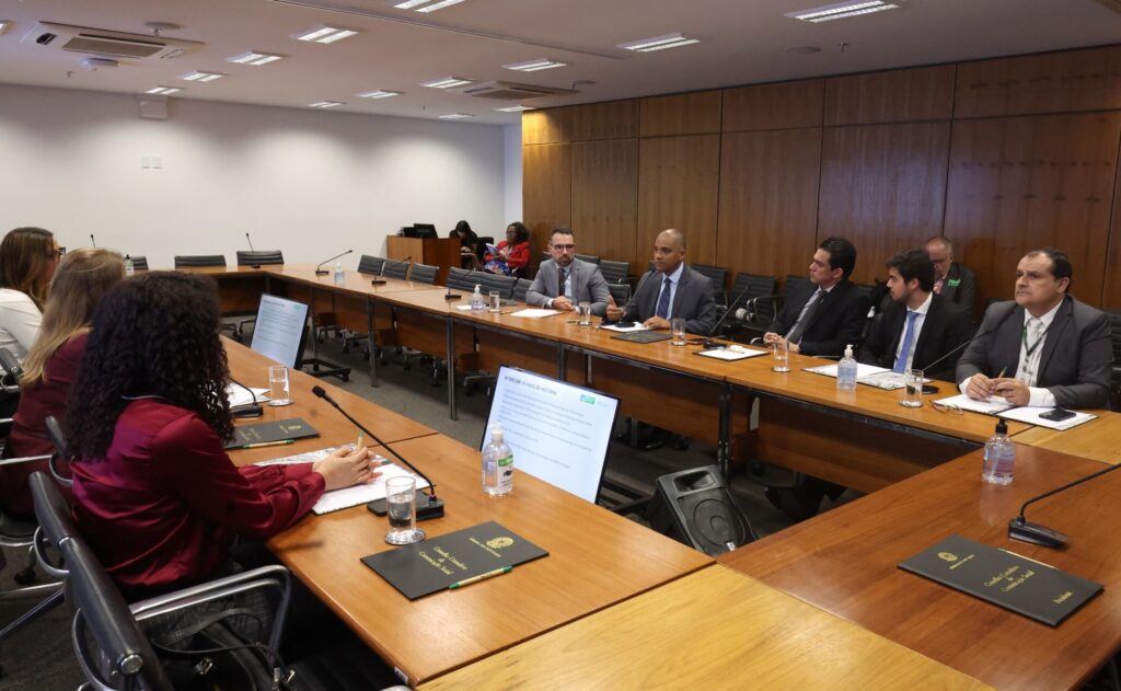 Reunião do Conselho de Comunicação Social com participantes sentados ao redor de mesas de madeira em sala corporativa.