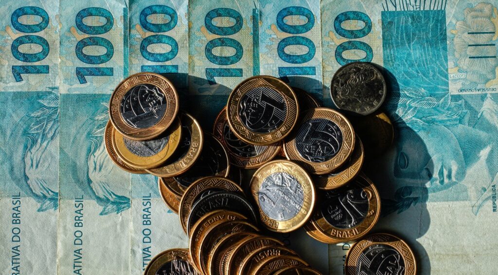 orçamento público: cédulas de cem reais e moedas brasileiras empilhadas sobre uma superfície.