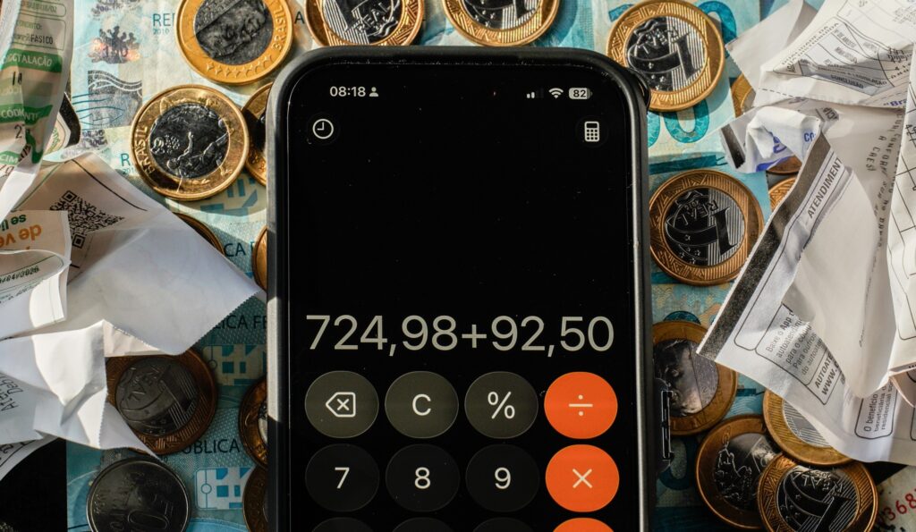 previa da inflacao: smartphone com calculadora sobre cédulas brasileiras e moedas de um real.