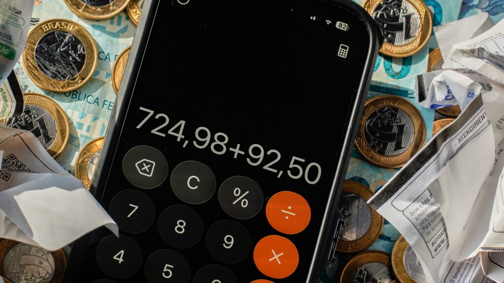 desenrola: smartphone com calculadora exibindo soma sobre cédulas de real, moedas e recibos.