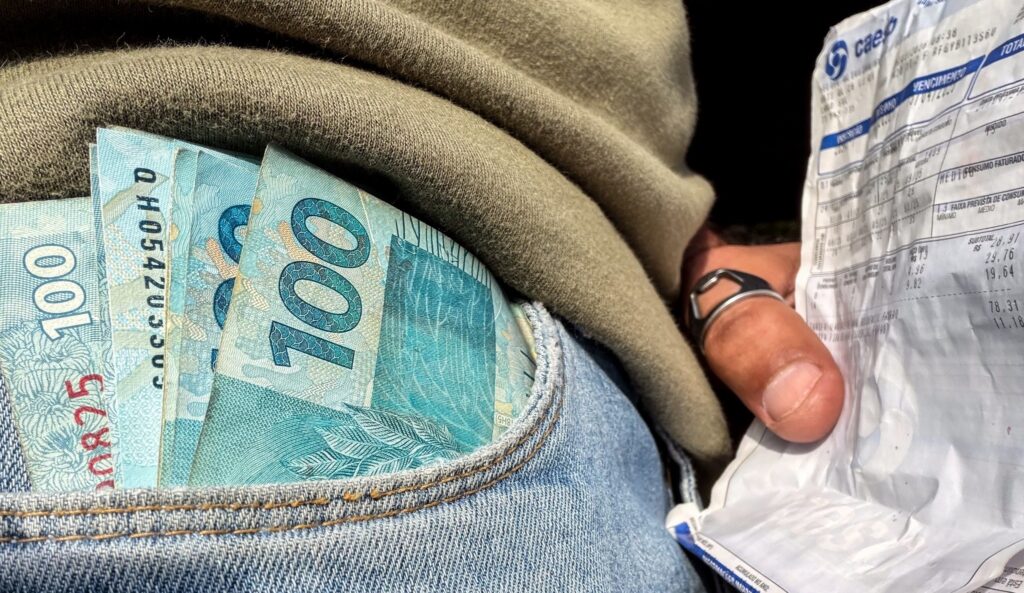 comércio varejista: cédulas de 100 reais em bolso de calça jeans e mão segurando boleto.
