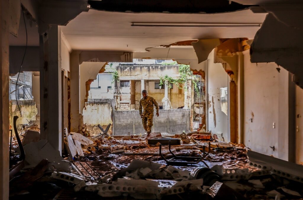 cota de alerta: Militar fardado caminha por entre escombros e lama no interior de um prédio destruído.