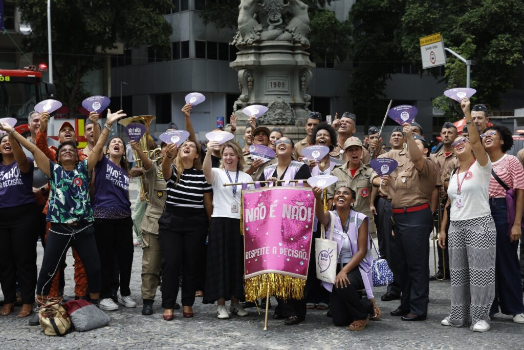 assédio eleitoral: Grupo de pessoas em praça pública segura faixas e placas de campanha contra o assédio.