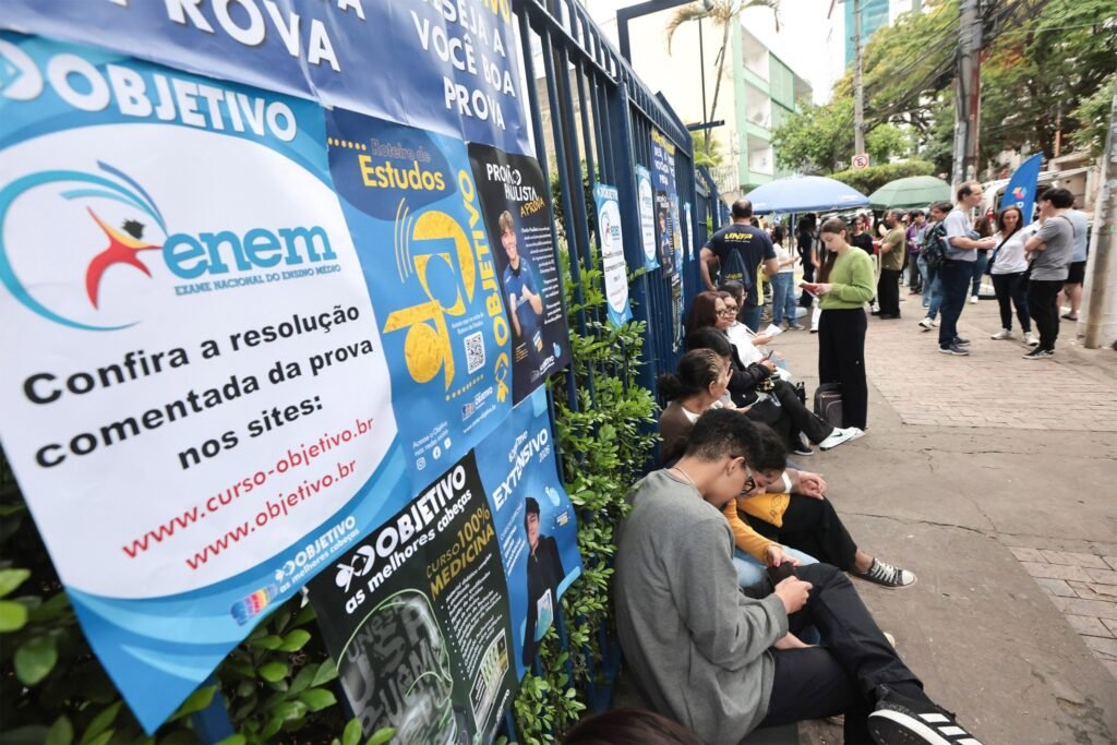 Enamed 2026: Estudantes aguardam em calçada ao lado de banners com indicação de exame nacional.