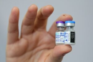 virus sincicial: mão segurando dois frascos da vacina Abrysvo da Pfizer.