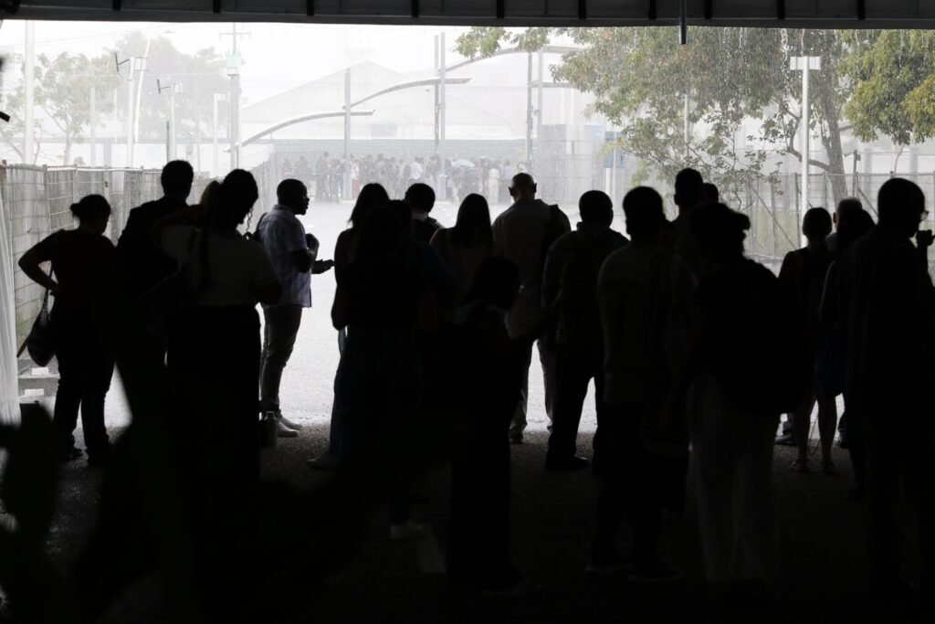 prevencao de desastres: pessoas aguardam sob um abrigo durante chuva forte em área externa.
