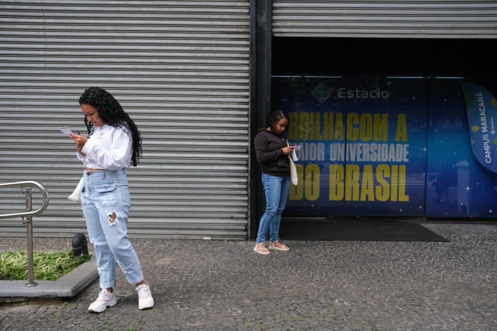 Revalida 2026/2: Duas jovens em uma calçada consultam papéis em frente a uma unidade da Universidade Estácio.