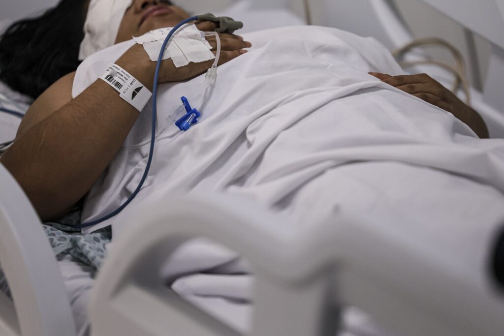André Janones: paciente em leito hospitalar com curativo nos olhos e acesso venoso no braço.