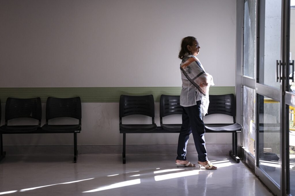hemofilia A: Mulher em pé em sala de espera de hospital, olhando para a porta ao lado de fileiras de cadeiras pretas.